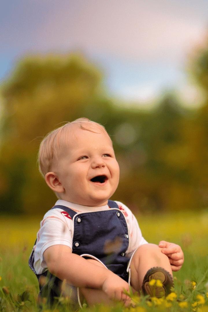 Em bé mặc yếm bò ngồi trên đồng cỏ xanh hoa vàng cười rạng rỡ như nắng mai